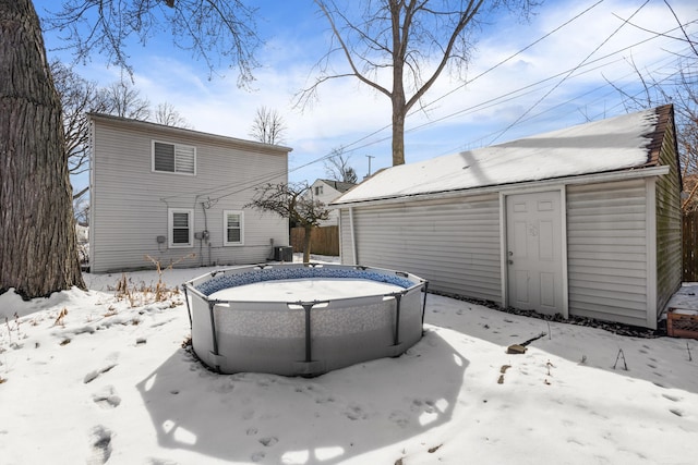 snow covered house featuring fence, an outdoor pool, and an outdoor structure