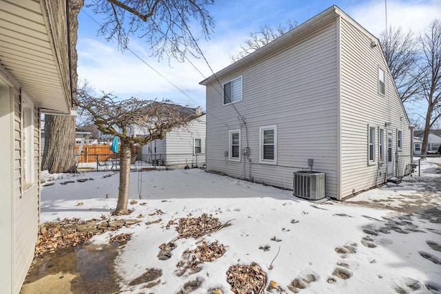 view of snow covered exterior featuring central AC and fence