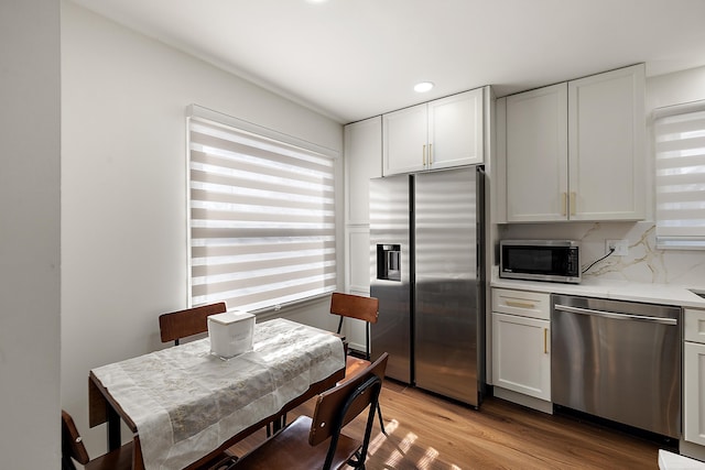 kitchen featuring appliances with stainless steel finishes, white cabinetry, light wood-style floors, and decorative backsplash