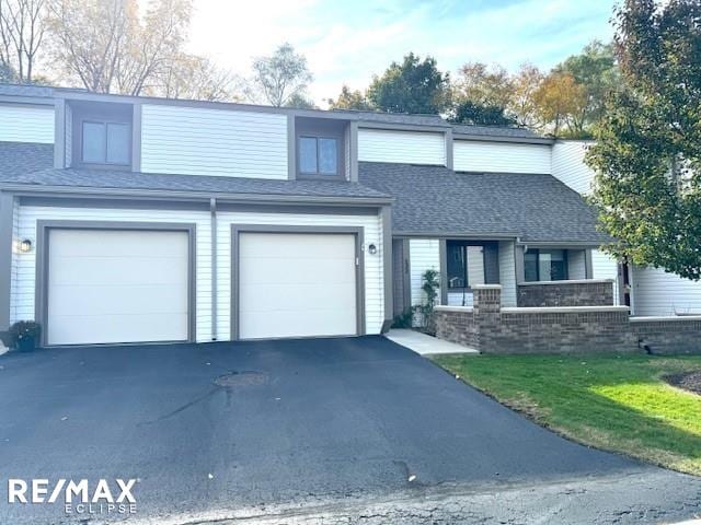 view of front of property featuring a garage, aphalt driveway, roof with shingles, a front yard, and brick siding