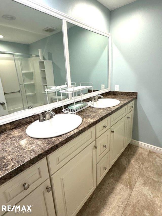 bathroom featuring double vanity, a sink, visible vents, and baseboards