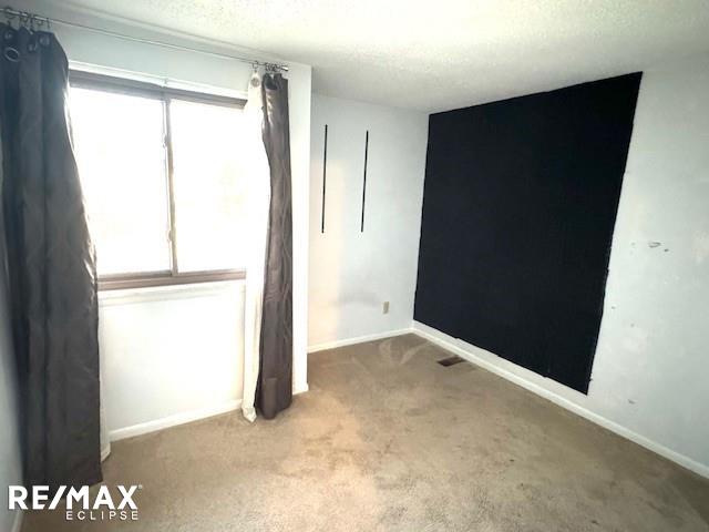 carpeted spare room with a textured ceiling and baseboards