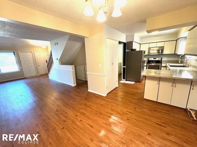 kitchen featuring a textured ceiling, stainless steel appliances, wood finished floors, a sink, and open floor plan