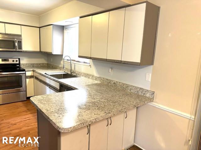 kitchen featuring a peninsula, stainless steel appliances, light countertops, light wood-type flooring, and a sink