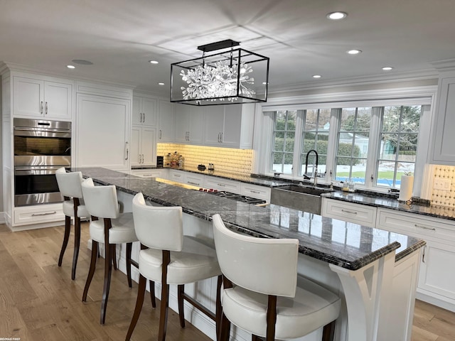 kitchen with light wood finished floors, backsplash, double oven, white cabinets, and a sink