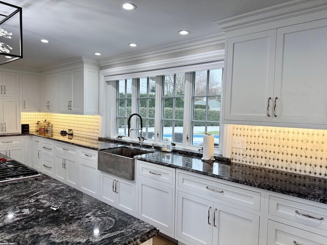 kitchen with tasteful backsplash, dark stone countertops, white cabinets, and a sink