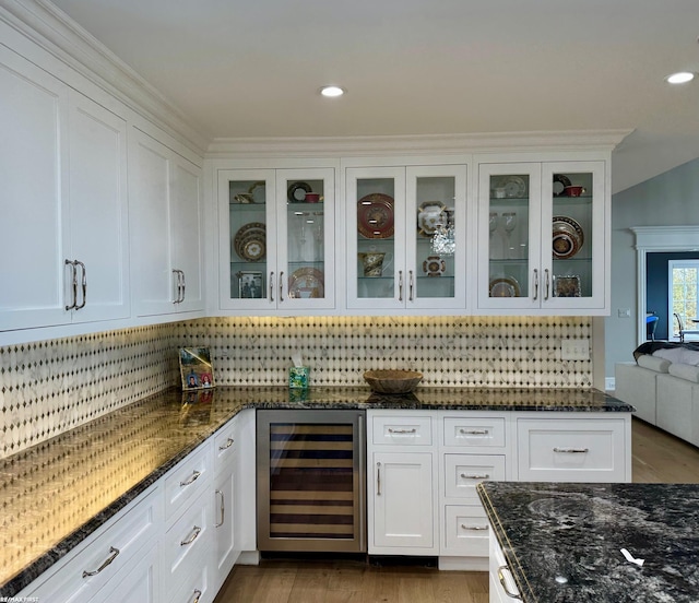 kitchen featuring decorative backsplash, glass insert cabinets, white cabinets, dark stone countertops, and beverage cooler