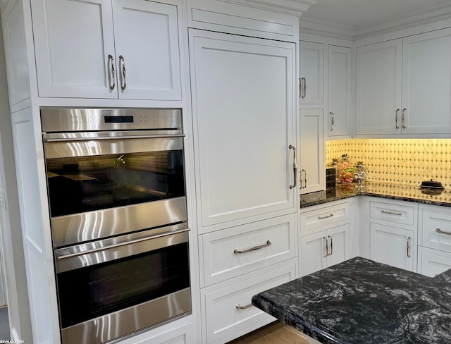 kitchen with double oven, white cabinetry, decorative backsplash, and dark stone counters