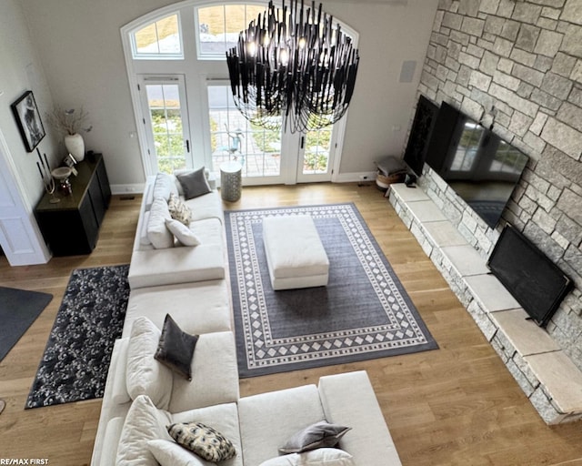 living room with a notable chandelier, a stone fireplace, wood finished floors, and baseboards