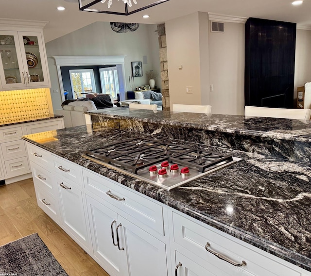 kitchen with light wood-style flooring, stainless steel gas cooktop, visible vents, open floor plan, and dark stone countertops