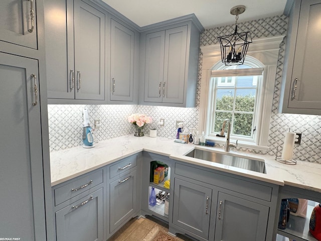 kitchen featuring light stone counters, decorative light fixtures, tasteful backsplash, gray cabinetry, and a sink