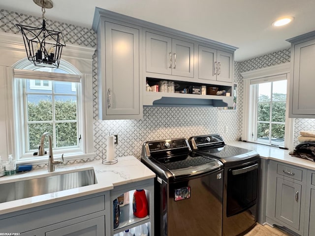 washroom featuring independent washer and dryer, cabinet space, a sink, and a notable chandelier