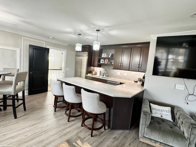 kitchen with tasteful backsplash, a breakfast bar, hanging light fixtures, light countertops, and dark brown cabinets