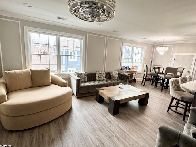 living room with crown molding, light wood-style floors, a notable chandelier, and a decorative wall