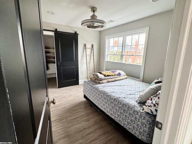 bedroom featuring a barn door, wood finished floors, visible vents, and baseboards