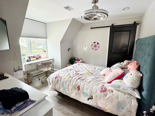 bedroom featuring a barn door, visible vents, and wood finished floors