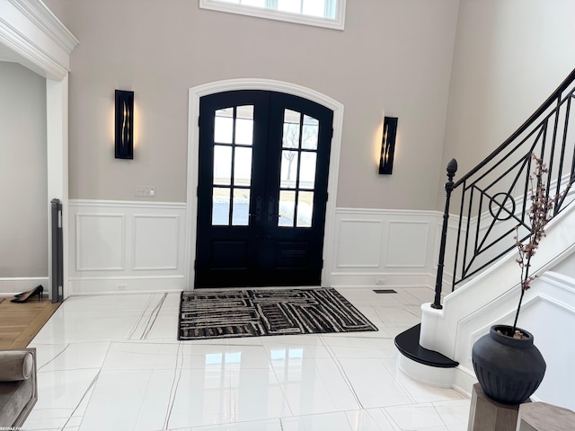 tiled entrance foyer featuring a wainscoted wall, plenty of natural light, stairs, and french doors