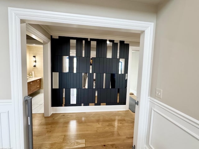 entryway with ornamental molding, a decorative wall, wood finished floors, and wainscoting