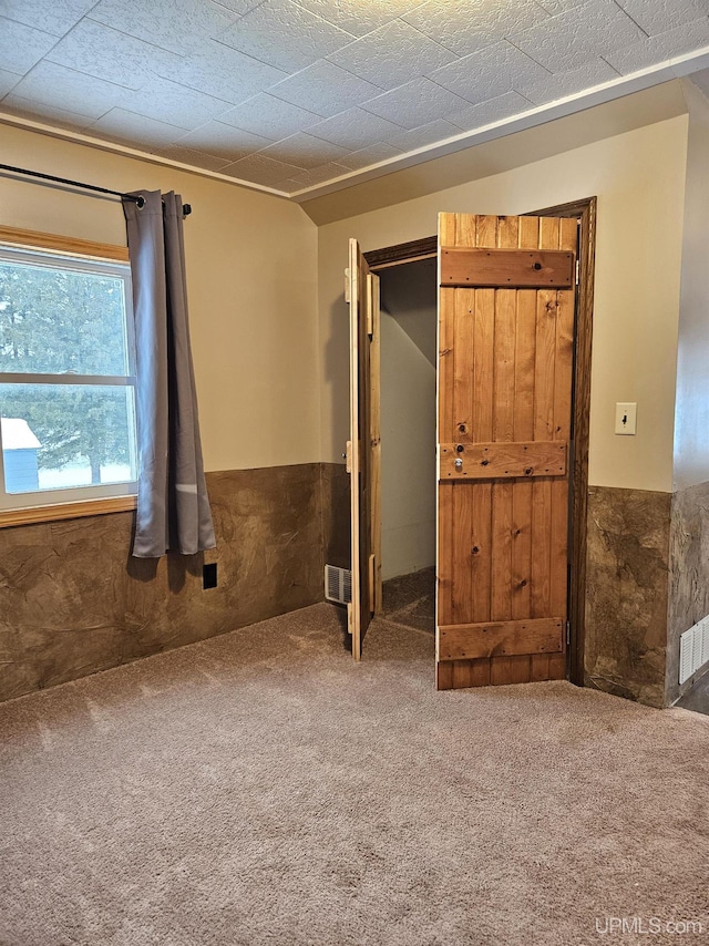 interior space with a wainscoted wall, carpet floors, and visible vents