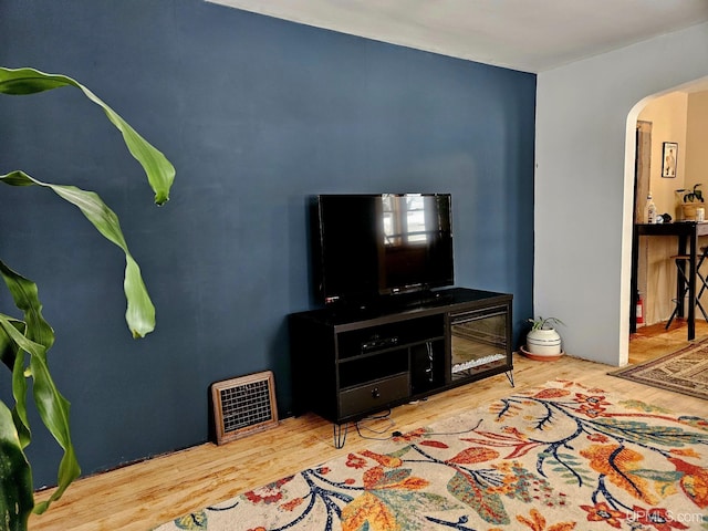 living room featuring arched walkways, wood finished floors, and visible vents