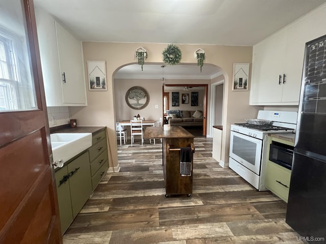 kitchen featuring arched walkways, white gas stove, freestanding refrigerator, dark countertops, and dark wood finished floors