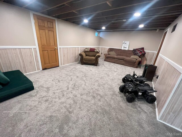 carpeted living area with a wainscoted wall and wooden walls