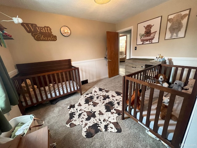 carpeted bedroom with a wainscoted wall and a textured ceiling