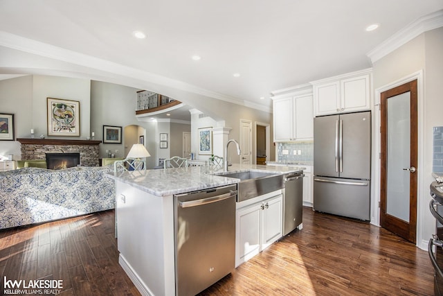 kitchen with a stone fireplace, appliances with stainless steel finishes, a sink, and white cabinetry