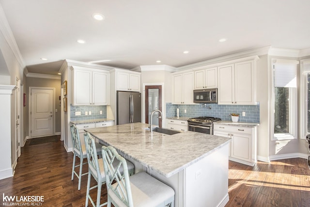 kitchen with a sink, dark wood finished floors, white cabinets, appliances with stainless steel finishes, and a kitchen bar