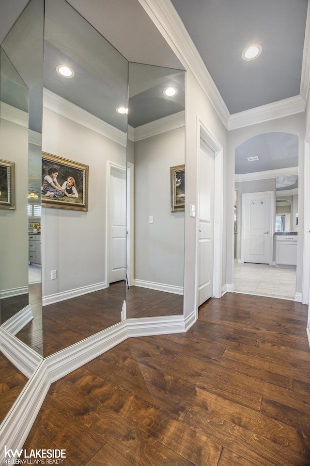 foyer with ornamental molding, arched walkways, baseboards, and wood finished floors