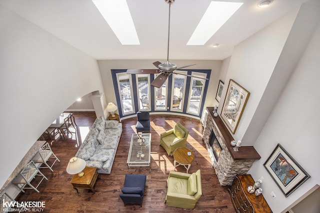 living room featuring a skylight, arched walkways, a ceiling fan, wood finished floors, and high vaulted ceiling