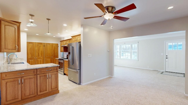 kitchen with light colored carpet, stainless steel appliances, a sink, light stone countertops, and pendant lighting