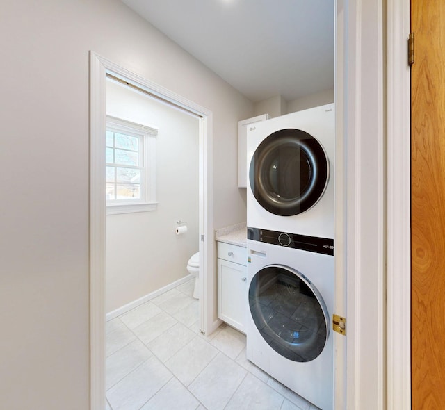 washroom featuring baseboards, laundry area, light tile patterned flooring, and stacked washer / drying machine