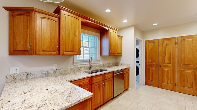 kitchen with stacked washer and dryer, brown cabinets, light stone countertops, stainless steel dishwasher, and a sink