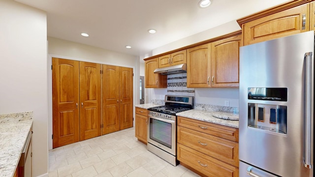 kitchen with light stone counters, brown cabinets, stainless steel appliances, under cabinet range hood, and recessed lighting