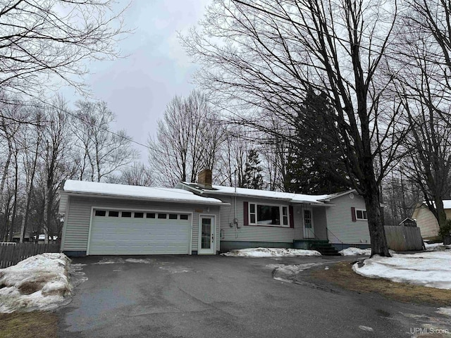 view of front of house featuring aphalt driveway, fence, a chimney, and an attached garage