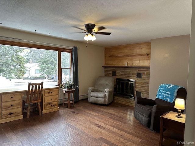 interior space featuring a ceiling fan, dark wood-style flooring, a stone fireplace, and a textured ceiling