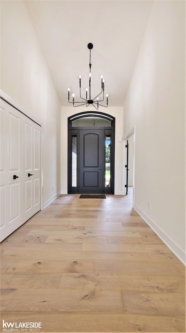 entryway featuring high vaulted ceiling, a chandelier, baseboards, and wood finished floors