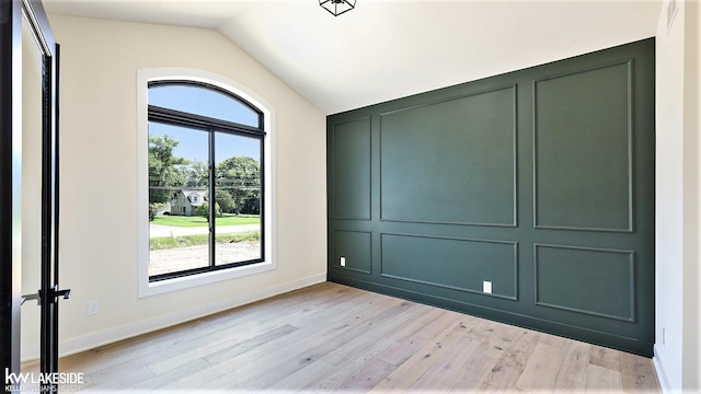 spare room featuring visible vents, baseboards, lofted ceiling, light wood-type flooring, and a decorative wall