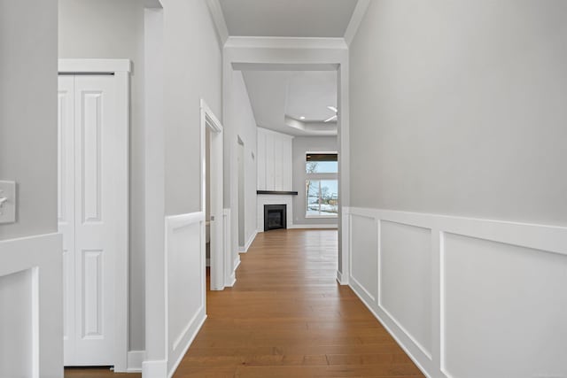 hallway with ornamental molding, wainscoting, a decorative wall, and wood finished floors