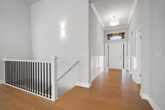 hall with a decorative wall, wood finished floors, an upstairs landing, wainscoting, and crown molding