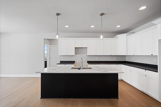 kitchen with light wood-style flooring, a kitchen island with sink, white cabinetry, and a sink