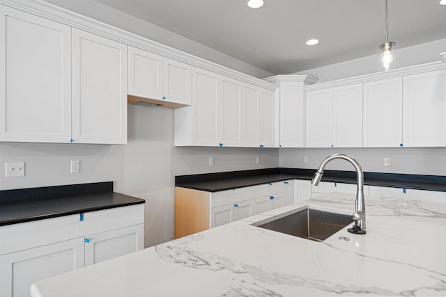 kitchen with light stone countertops, white cabinets, a sink, and decorative light fixtures