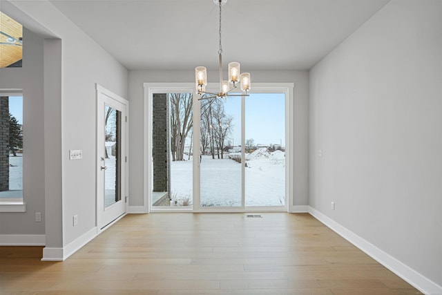 unfurnished dining area featuring baseboards, visible vents, light wood finished floors, and an inviting chandelier