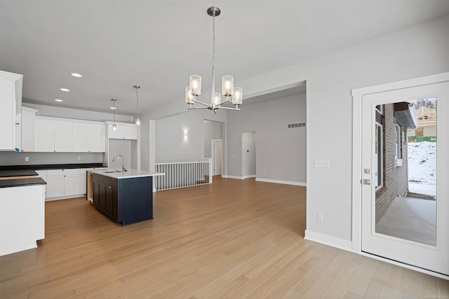 kitchen featuring white cabinets, hanging light fixtures, light wood-type flooring, a chandelier, and a sink