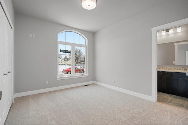 unfurnished bedroom with ensuite bathroom, light carpet, visible vents, baseboards, and a closet