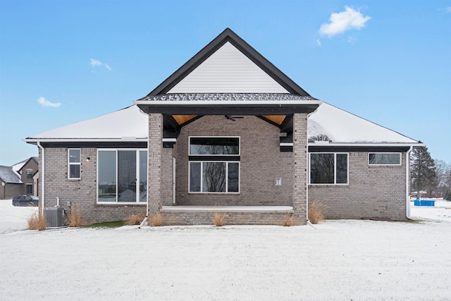 snow covered rear of property with brick siding and central air condition unit