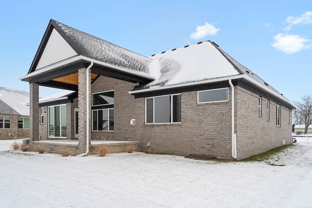 snow covered house featuring brick siding and a patio