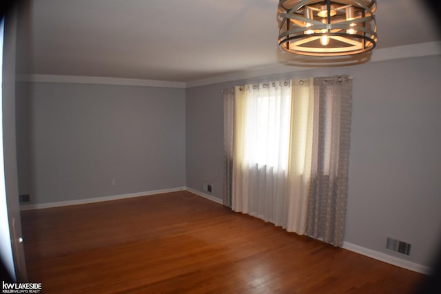 empty room featuring visible vents, crown molding, baseboards, and wood finished floors