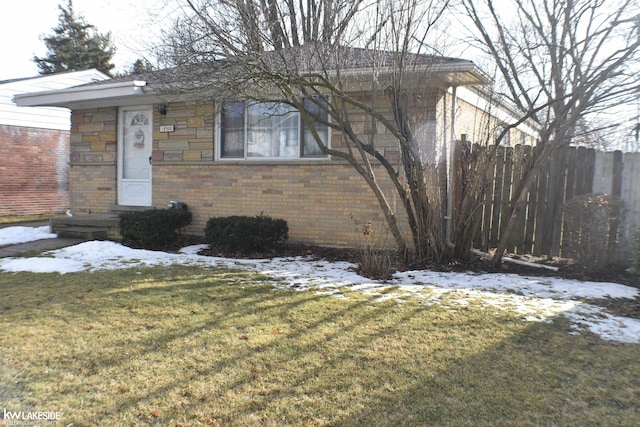 ranch-style house with a yard, stone siding, fence, and brick siding